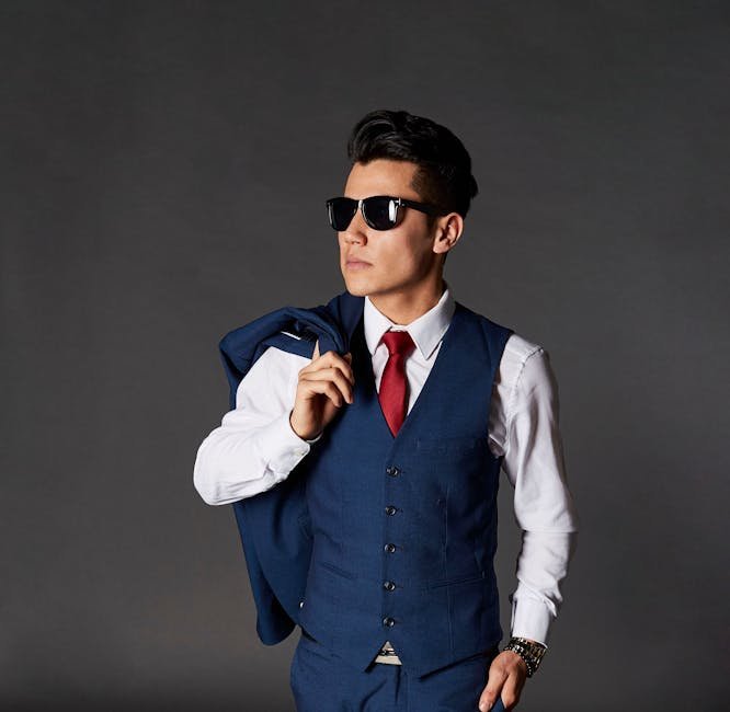 Portrait of a stylish man in a blue suit and sunglasses posing confidently indoors.